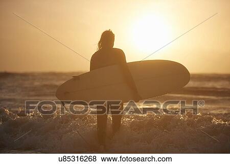 Silhouette of young male surfer carrying surfboard in sea, Devon, England, UK View Large Photo Image Stock Photo - Silhouette of young male surfer carrying surfboard in sea, Devon, England, UK. Fotosearch