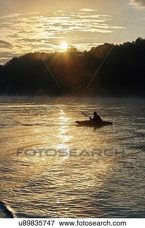 Stock Photo - Silhouetted kayaker on Wimbleball lake at sunrise, Exmoor, Somerset, England. Fotosearch