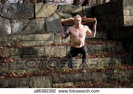 Tattooed mid adult man carrying tree branch on shoulders doing lunges on stone steps View Large Photo Image Stock Image - Tattooed mid adult man carrying tree branch on shoulders doing lunges on stone steps. Fotosearch