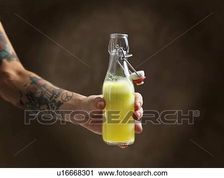 Stock Image - Tattooed womans arm holding raw juice in glass bottle. Fotosearch