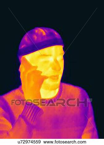 Stock Photo - Thermal image of young man wearing face mask and hat using smartphone. Fotosearch