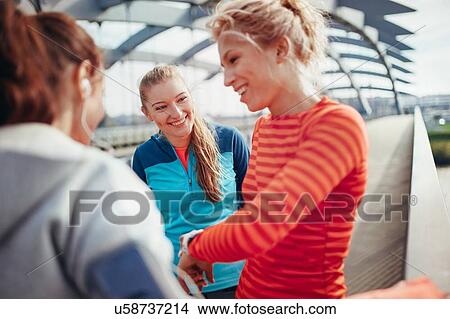 Picture - Three female runners checking time on city footbridge. Fotosearch