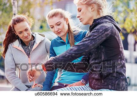 Picture - Three female runners coordinating times on smartwatch in city. Fotosearch