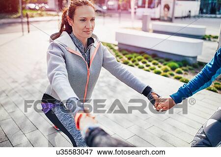 Three female runners holding hands whilst doing warm up exercises in city View Large Photo Image Stock Photo - Three female runners holding hands whilst doing warm up exercises in city. Fotosearch