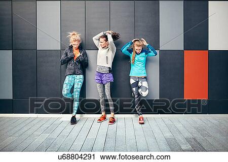 Stock Image - Three female runners putting up their hair in city underpass. Fotosearch