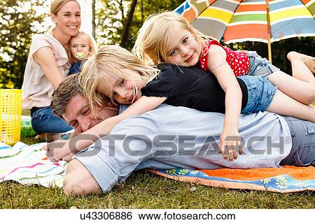 Two daughters lying on top of father at family picnic in park View Large Photo Image Stock Photograph - Two daughters lying on top of father at family picnic in park. Fotosearch