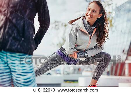 Stock Image - Two female runners doing warm up stretches in city. Fotosearch
