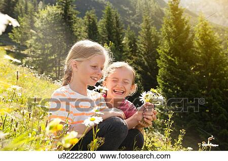Stock Image - Two young girls in field, picking flowers. Fotosearch