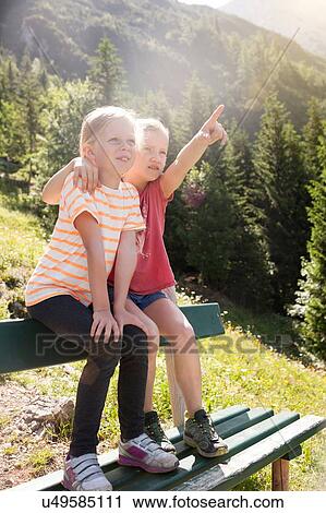 Two young girls sitting on bench, rural environment, looking at view View Large Photo Image Stock Image - Two young girls sitting on bench, rural environment, looking at view. Fotosearch