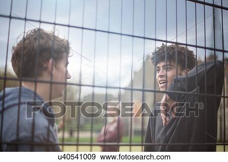 Stock Photo - Two young men leaning against fence, talking. Fotosearch