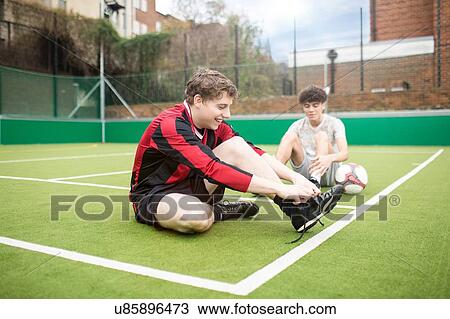 Stock Image - Two young men on urban football pitch, tying shoelaces. Fotosearch
