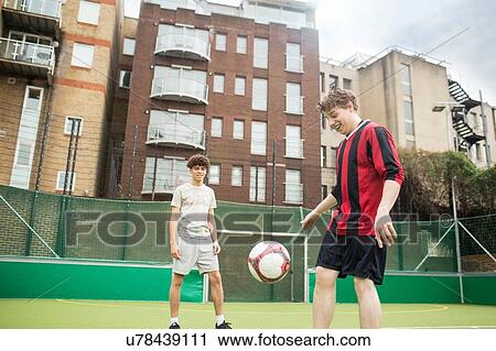 Stock Image - Two young men playing football on urban football pitch. Fotosearch