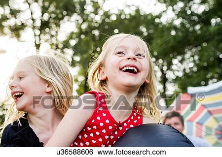 Two young sisters playing on inflatable in park View Large Photo Image Stock Photograph - Two young sisters playing on inflatable in park. Fotosearch