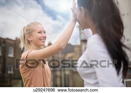 Stock Photograph - Two young women giving high five, outdoors. Fotosearch