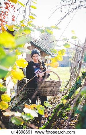 View through leaves of young woman in garden wearing knit hat holding wickerwork basket looking at camera smiling View Large Photo Image Stock Image - View through leaves of young woman in garden wearing knit hat holding wickerwork basket looking at camera smiling. Fotosearch