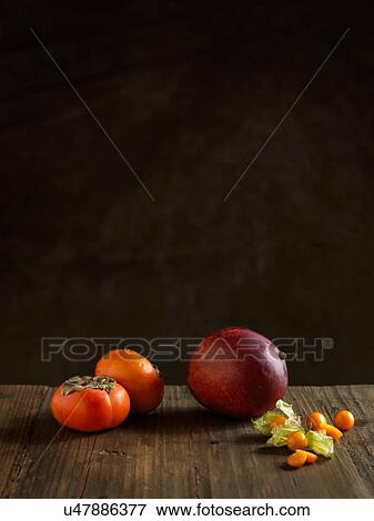 Whole mango and persimmons on wood table against dark background View Large Photo Image Stock Photo - Whole mango and persimmons on wood table against dark background. Fotosearch