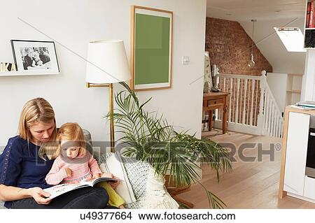 Woman and toddler daughter reading book on living room sofa View Large Photo Image Picture - Woman and toddler daughter reading book on living room sofa. Fotosearch
