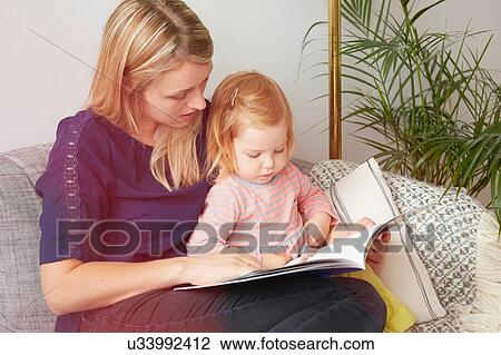 Stock Image - Woman and toddler daughter reading on living room sofa. Fotosearch