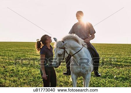 Stock Image - Woman chatting with man riding grey horse in field. Fotosearch