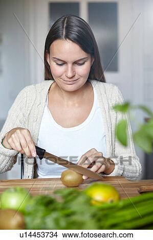 Picture - Woman cutting green kiwi on wooden table. Fotosearch