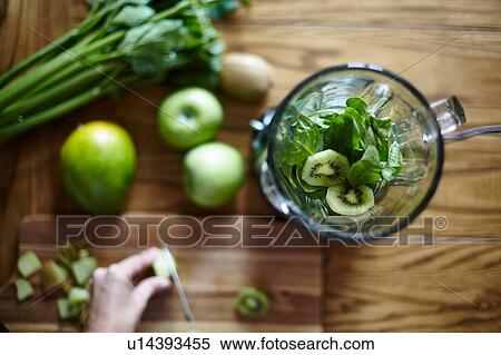 Stock Photography - Woman cutting green kiwi on wooden table. Fotosearch