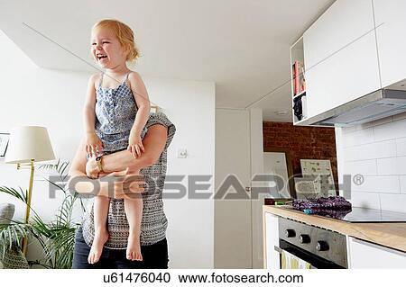 Stock Image - Woman lifting up toddler daughter in kitchen. Fotosearch
