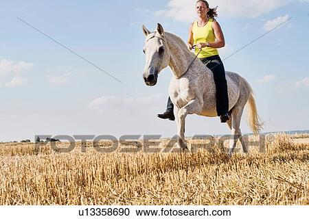Stock Image - Woman riding grey horse bareback in field. Fotosearch