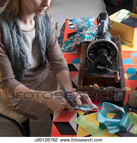 Stock Image - Woman with vintage sewing machine cutting ribbon at table. Fotosearch
