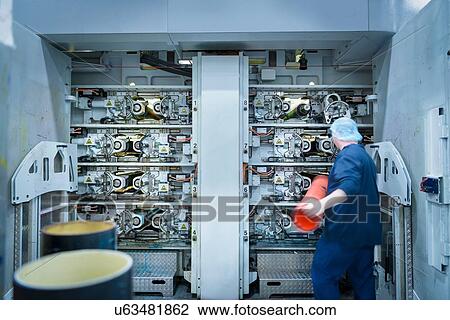 Stock Image - Worker loading printing plates into printer in food packaging printing factory. Fotosearch