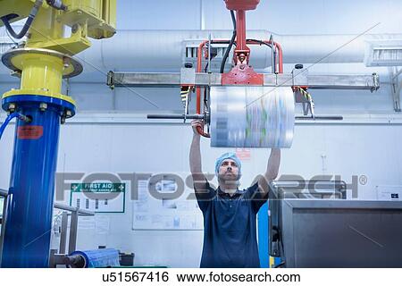 Stock Photograph - Worker moving roll of packaging in food packaging printing factory. Fotosearch