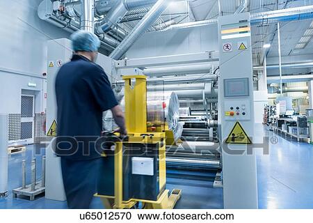 Stock Image - Worker unloading printed roll in food packaging printing factory. Fotosearch