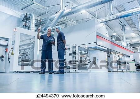 Stock Image - Workers with printing machine in food packaging printing factory. Fotosearch