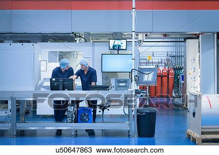 Stock Image - Workers with printing machine in food packaging printing factory. Fotosearch