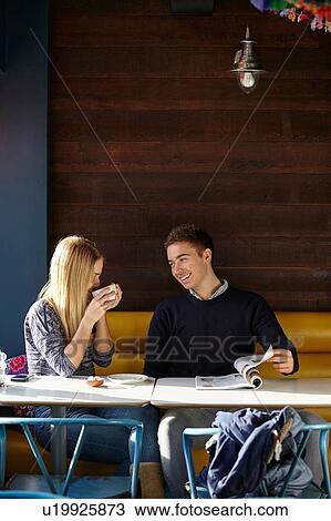 Stock Image - Young couple on date in cafe drinking coffee and reading magazine. Fotosearch