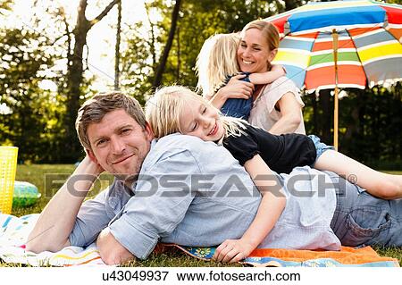 Stock Photo - Young daughter lying on top of father at family picnic in park. Fotosearch