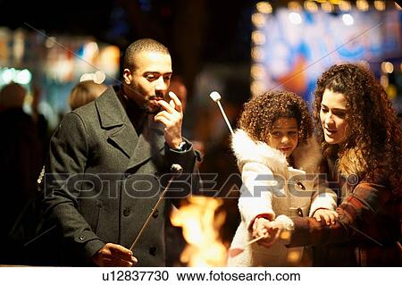 Stock Image - Young family at funfair, eating toasted marshmallows. Fotosearch