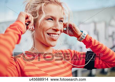Young female runner adjusting earphones in city View Large Photo Image Picture - Young female runner adjusting earphones in city. Fotosearch