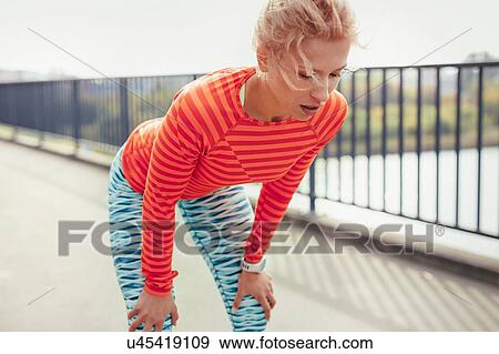Stock Photo - Young female runner taking a break on city footbridge. Fotosearch