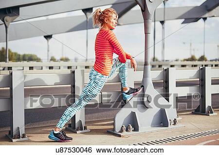 Stock Photograph - Young female runner warming up on city footbridge. Fotosearch