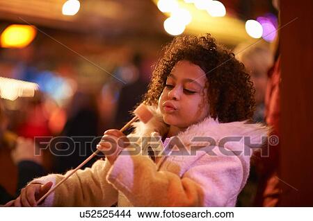 Picture - Young girl at funfair, blowing on toasted marshmellow. Fotosearch