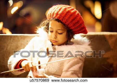 Stock Photo - Young girl, outdoors at night, holding marshmallows and skewer. Fotosearch