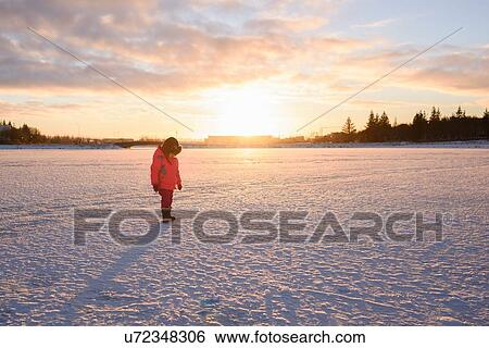 Stock Photograph - Young girl wearing red anorak looking down at snow covered field, Reykjavik, Iceland. Fotosearch