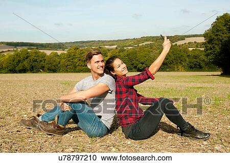 Young hiking couple sitting back to back in field taking smartphone selfie, Great Missenden, Buckinghamshire, U. K View Large Photo Image Stock Image - Young hiking couple sitting back to back in field taking smartphone selfie, Great Missenden, Buckinghamshire, U. K. Fotosearch