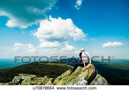 Picture - Young male hiker sitting on rock looking out over landscape, Russia. Fotosearch
