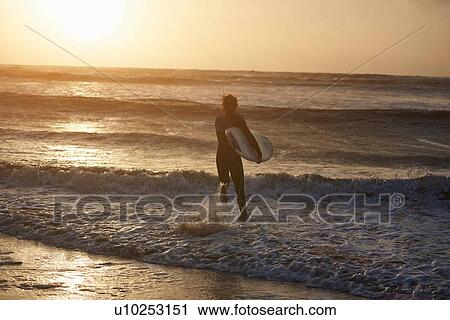 Young male surfer carrying surfboard running into sea, Devon, England, UK View Large Photo Image Stock Image - Young male surfer carrying surfboard running into sea, Devon, England, UK. Fotosearch