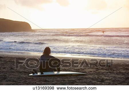 Young male surfer sitting looking out from beach, Devon, England, UK View Large Photo Image Stock Photo - Young male surfer sitting looking out from beach, Devon, England, UK. Fotosearch