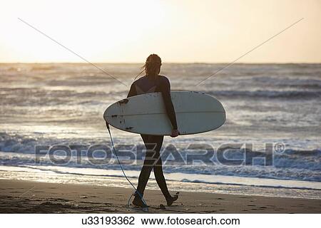 Young male surfer walking on beach carrying surfboard, Devon, England, UK View Large Photo Image Stock Image - Young male surfer walking on beach carrying surfboard, Devon, England, UK. Fotosearch