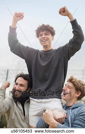 Stock Image - Young man being lifted in air by two friends, celebrating. Fotosearch