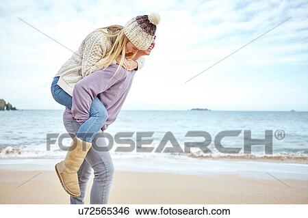 Young man giving girlfriend a piggyback on beach, Constantine Bay, Cornwall, UK View Large Photo Image Stock Photograph - Young man giving girlfriend a piggyback on beach, Constantine Bay, Cornwall, UK. Fotosearch