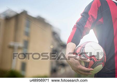 Stock Image - Young man holding football, mid section. Fotosearch